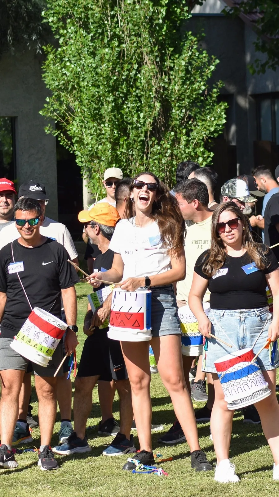 Grupo de participantes riendo y tocando tambores pintados en el parque durante una actividad de team building