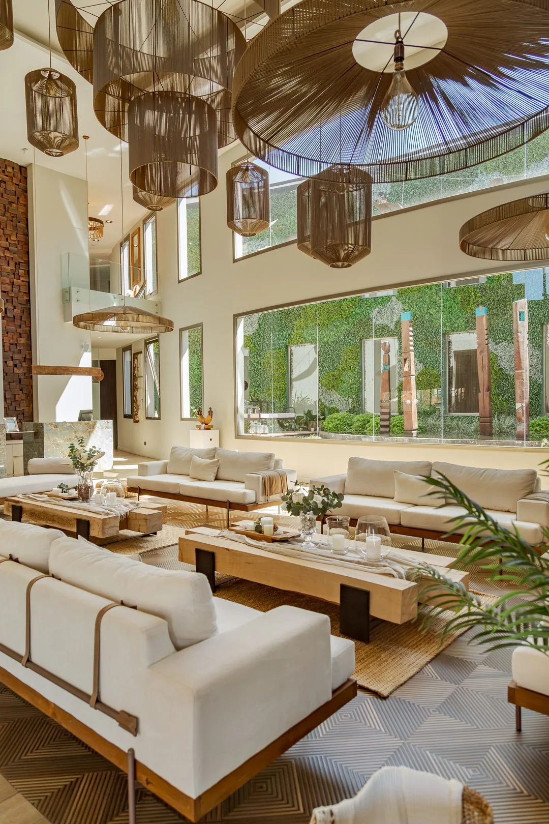 Hall de doble altura del hotel con sillones blancos, lámparas colgantes de fibra y jardín vertical detrás del ventanal