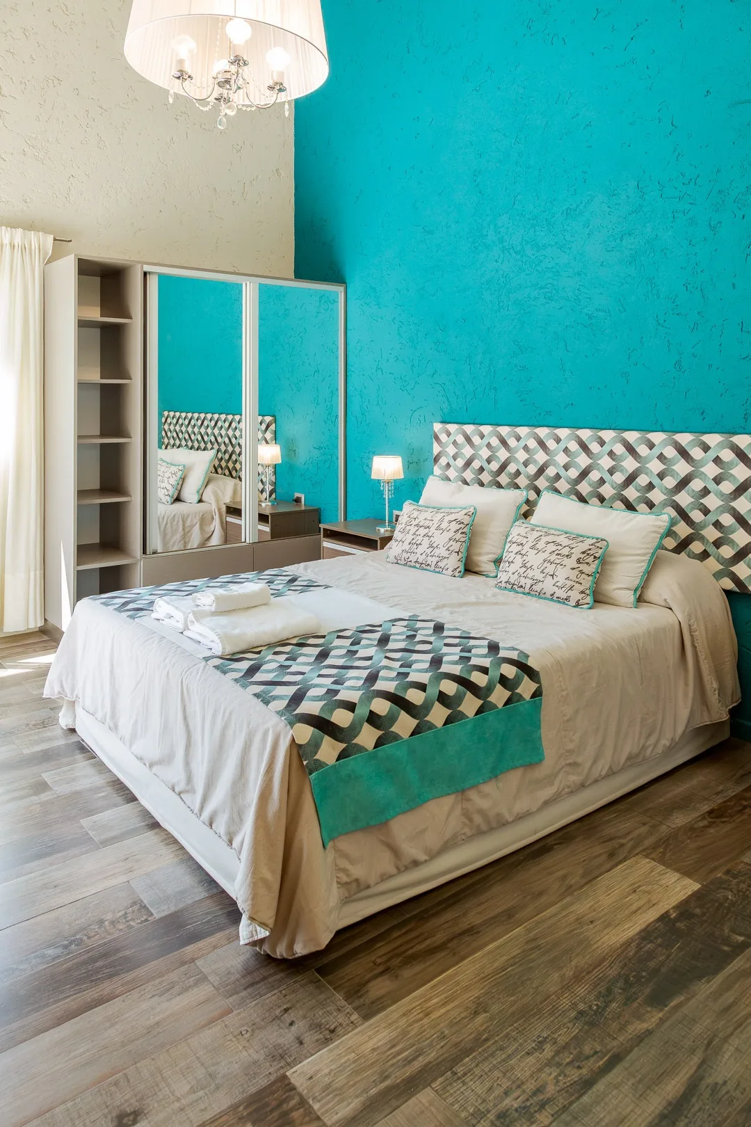 Dormitorio con cama matrimonial, pared turquesa, respaldo tejido y placard con espejo