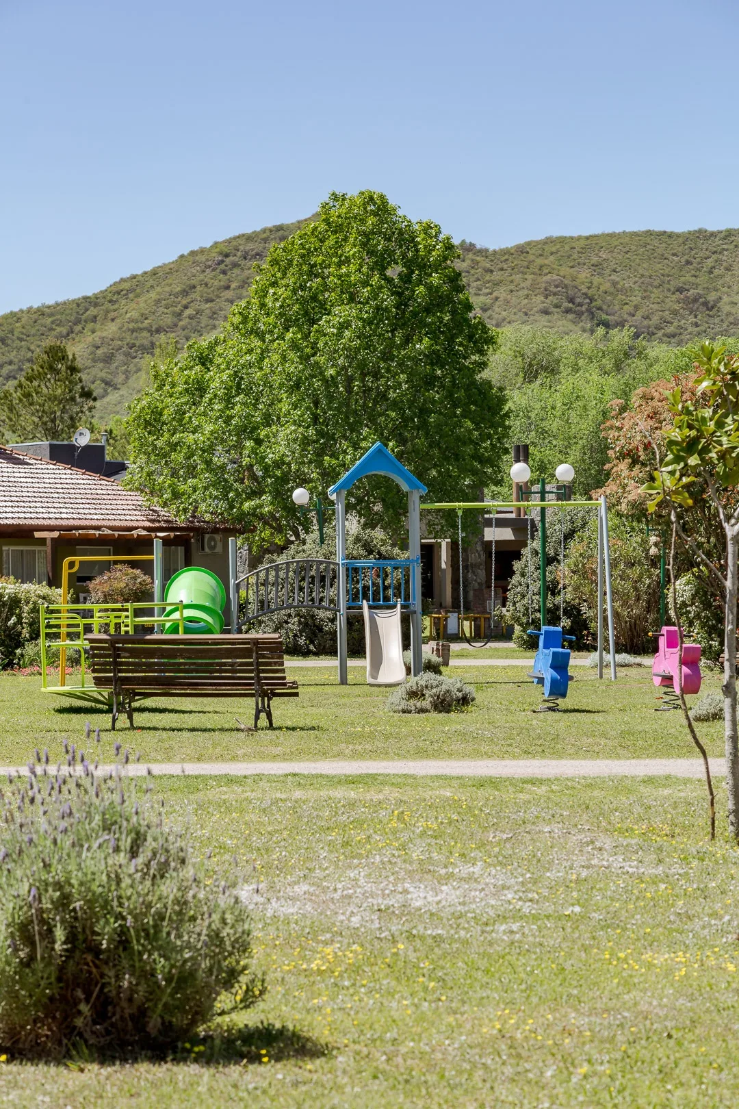 Plaza de juegos con tobogán, hamacas y juegos de resorte en el parque, con las sierras de fondo