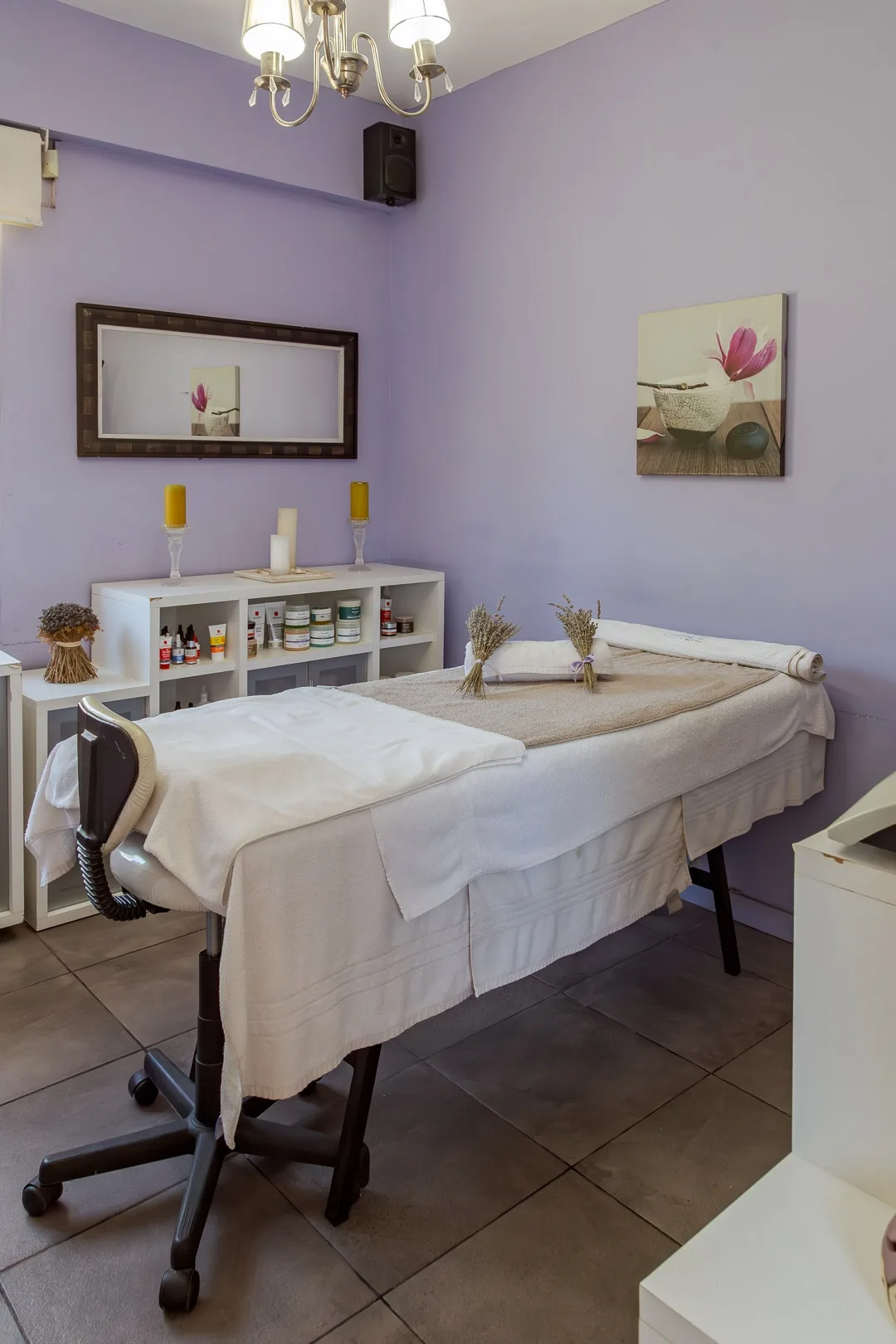 Gabinete del spa con camilla de masajes, paredes lila, velas y estantes con productos