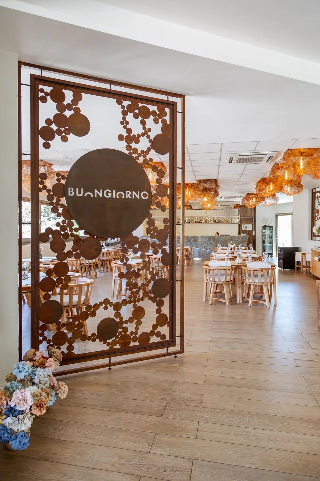 Entrada del restaurante Buongiorno con biombo calado de chapa y el logo, salón con mesas al fondo