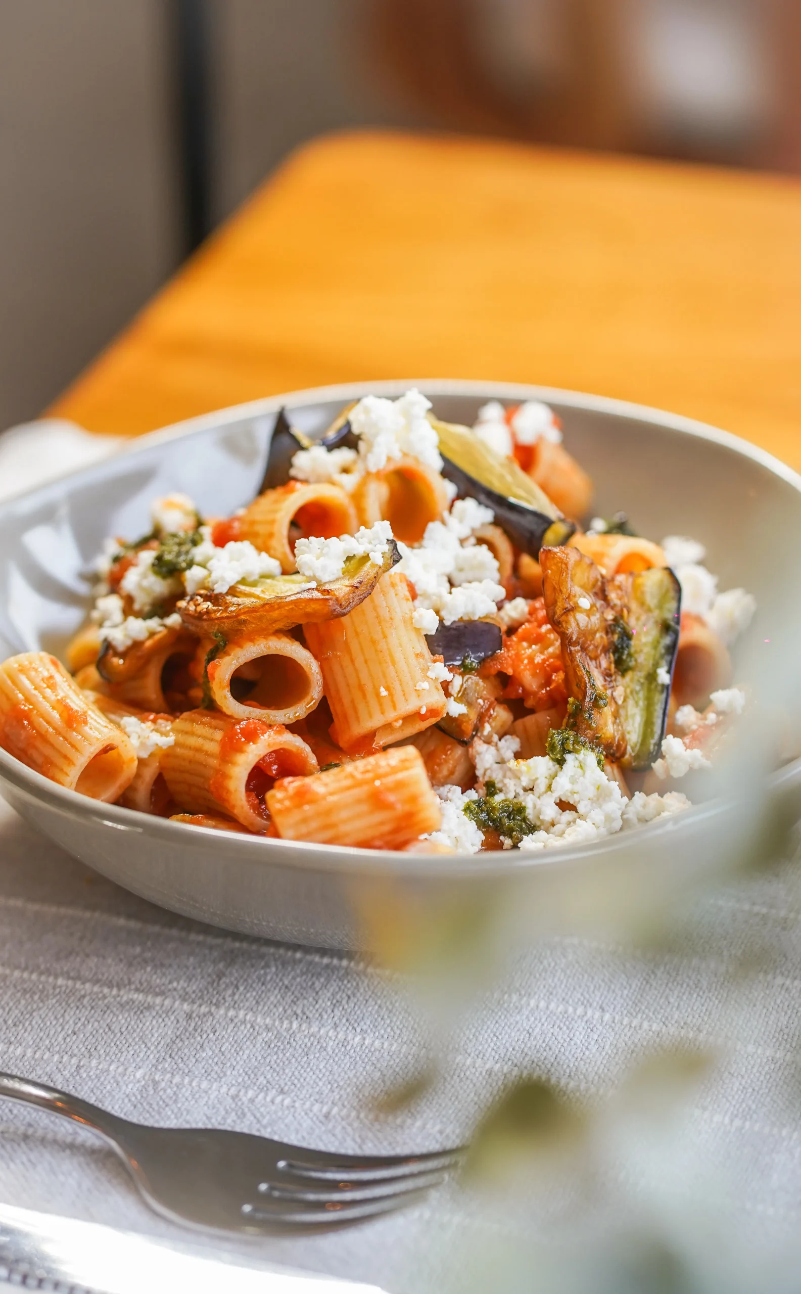 Plato de rigatoni con salsa de tomate, berenjenas y queso desmenuzado sobre la mesa