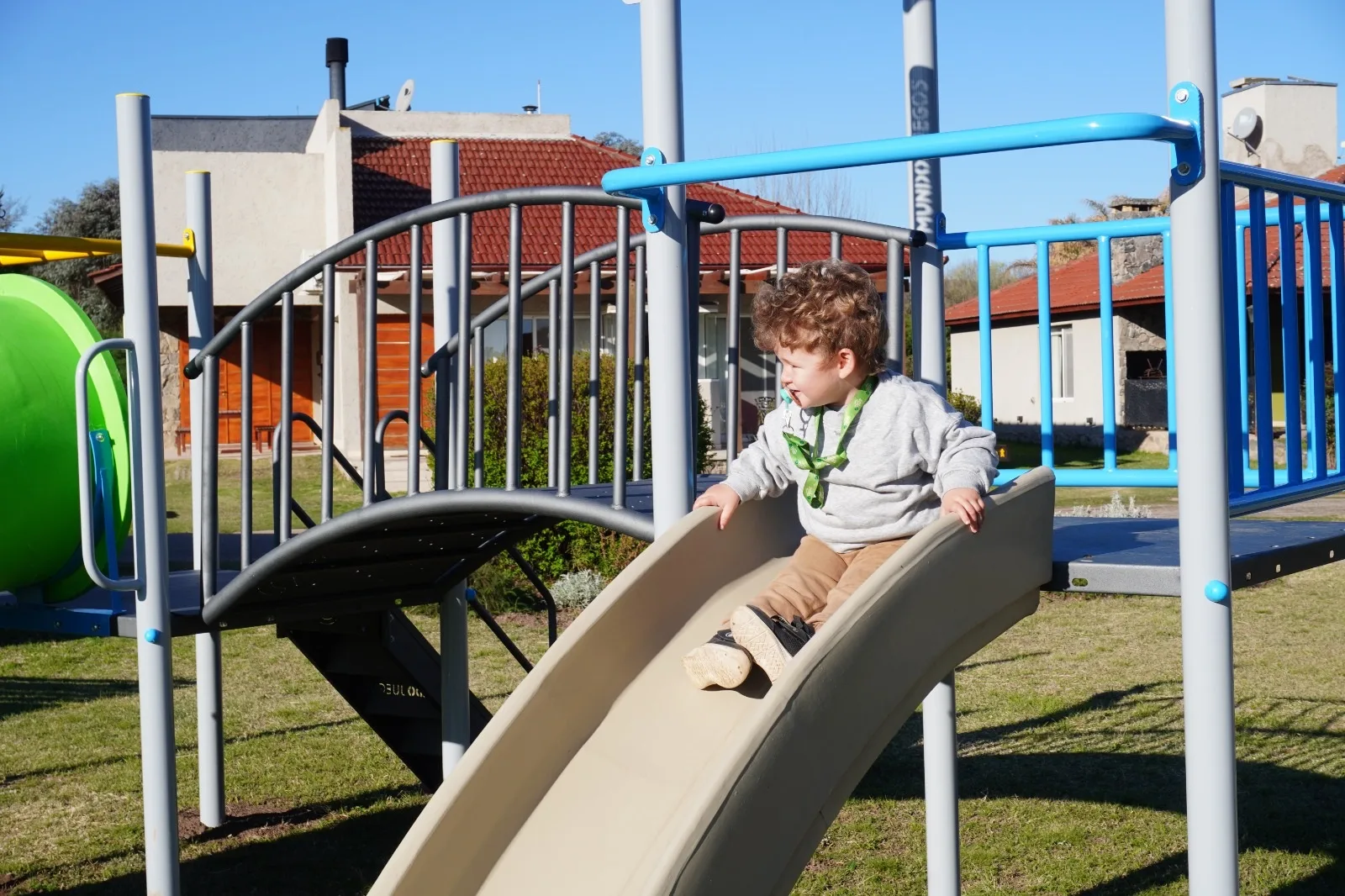 Nene bajando por el tobogán de la plaza de juegos, con casas de techo de tejas detrás