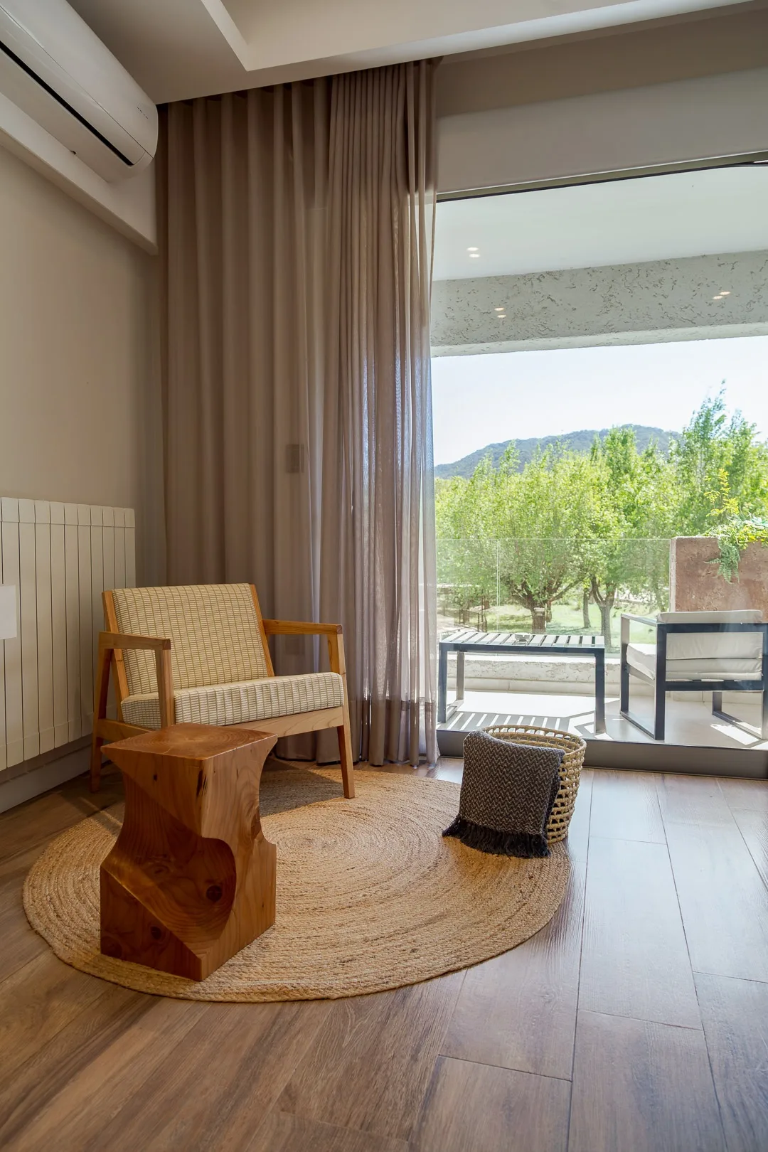 Rincón de una habitación del hotel con sillón y mesa de madera tallada, abierta a un balcón con vista a la arboleda