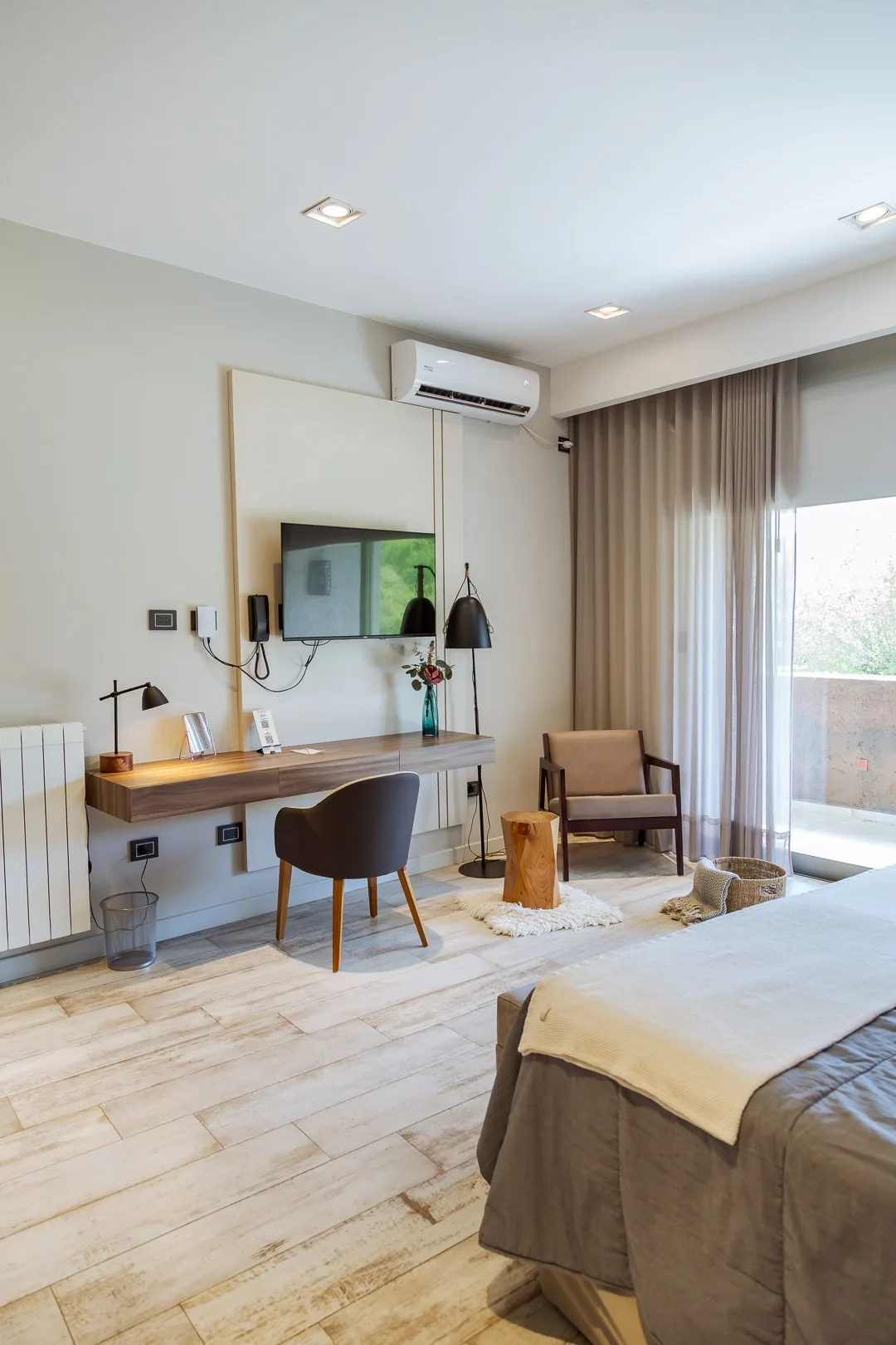 Habitación del hotel con escritorio, televisor, sillón y ventanal con cortinas