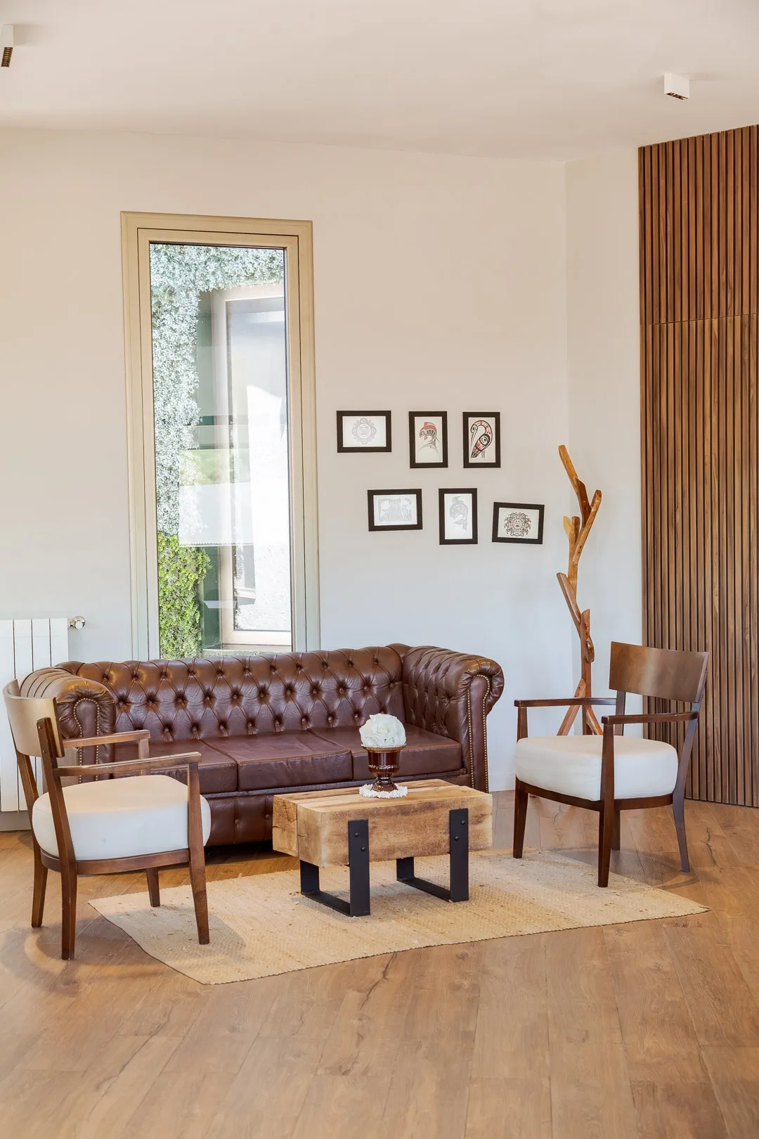 Espacio de estar del hotel con sillón Chesterfield de cuero, dos sillas, mesa ratona y cuadros