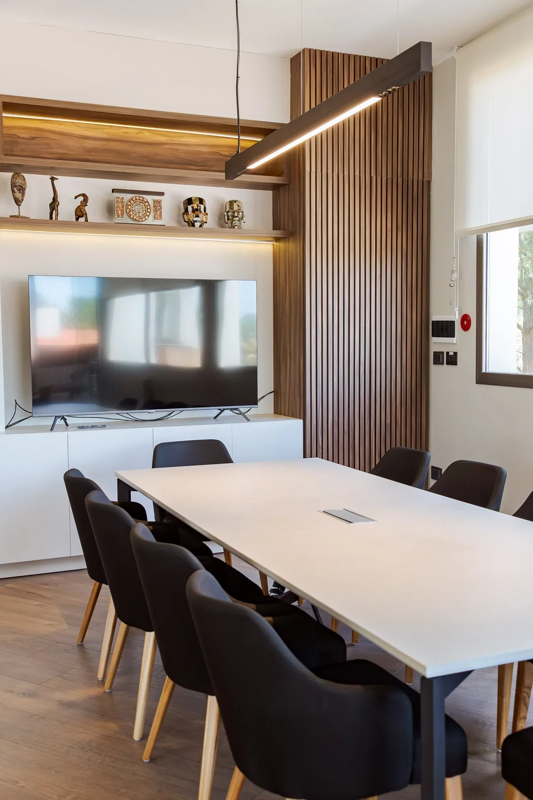 Sala de co-working y reuniones del hotel con mesa larga blanca, sillas negras y televisor