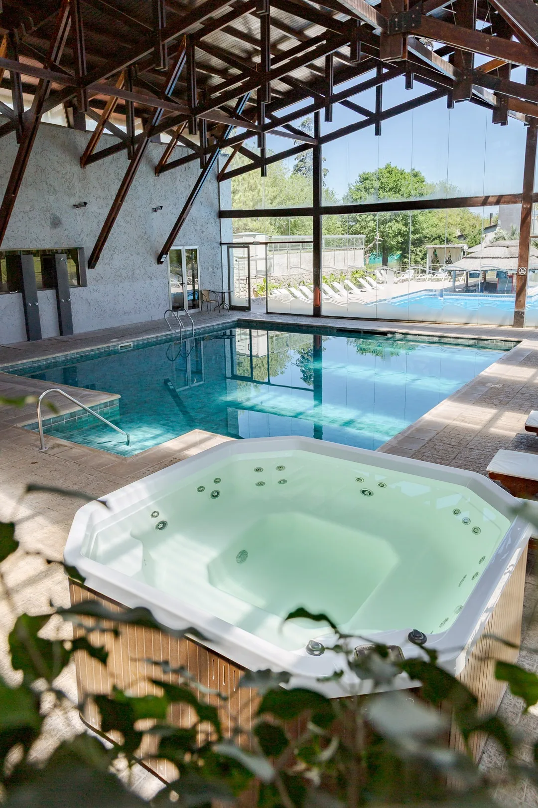 Jacuzzi en primer plano y la pileta climatizada cubierta, con un ventanal hacia la pileta exterior