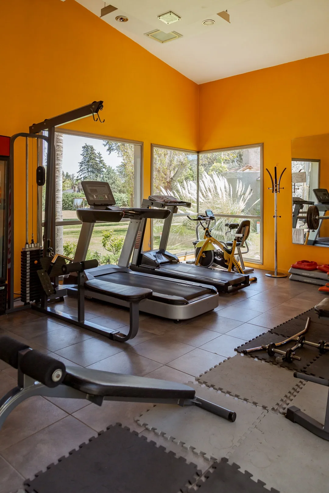 Gimnasio con cintas de correr, bicicleta y máquinas de musculación, paredes naranjas y ventanales
