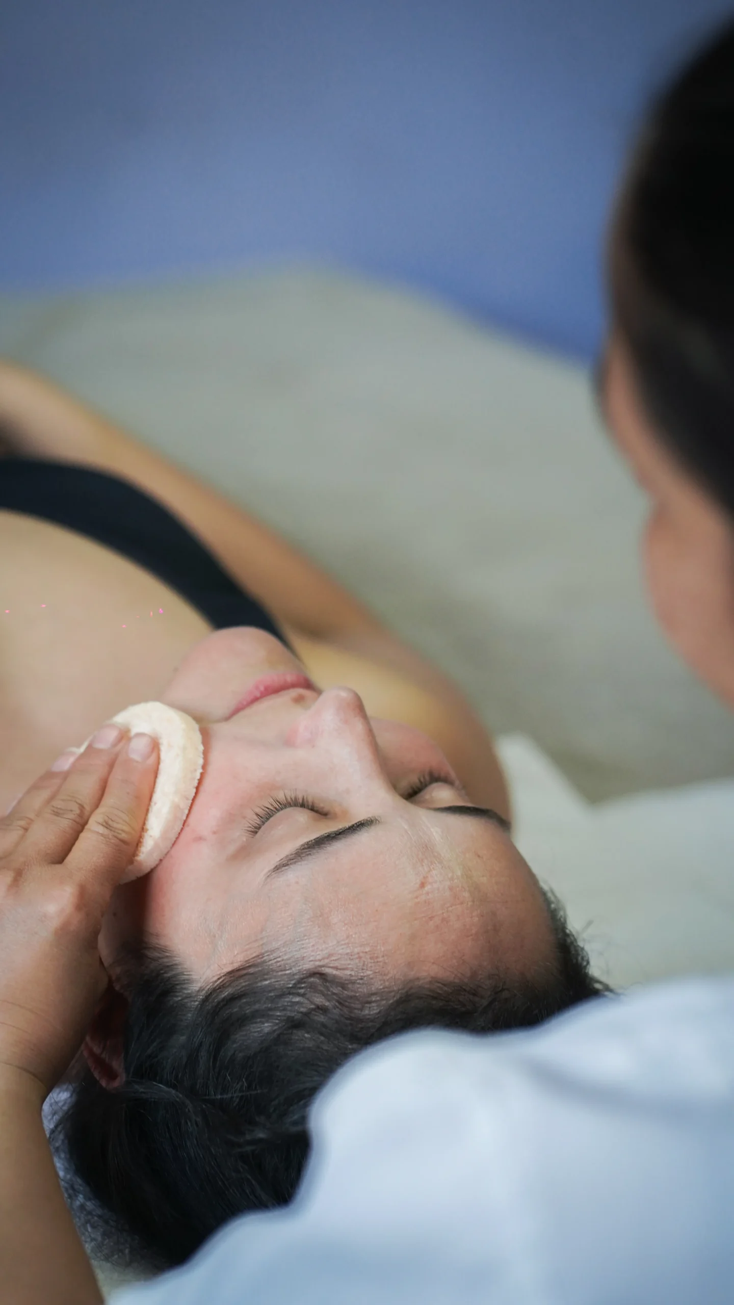 Primer plano de una mujer con los ojos cerrados mientras le hacen un tratamiento facial